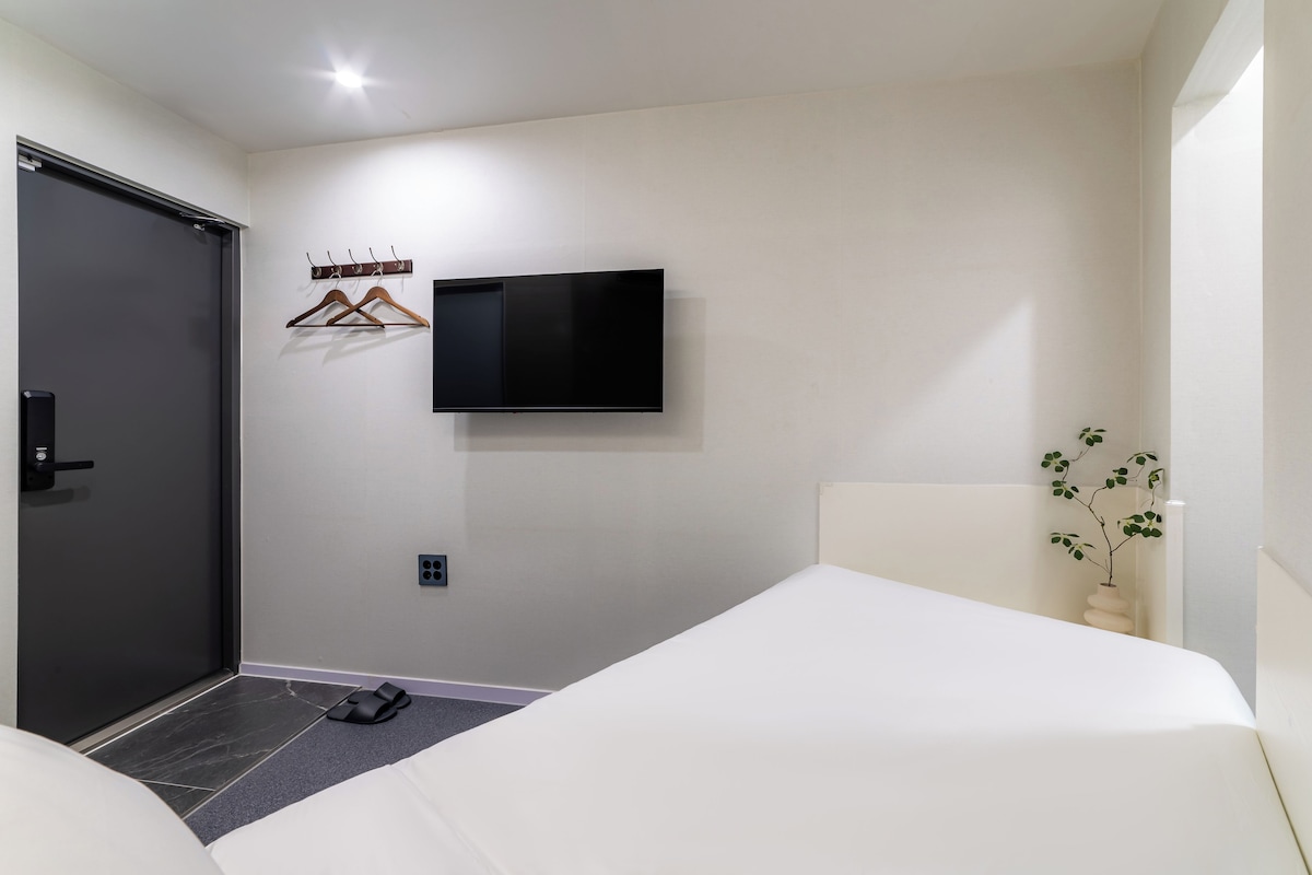 Une chambre d’hôtel avec un lit, un téléviseur fixé au mur, un porte-manteau et une porte.