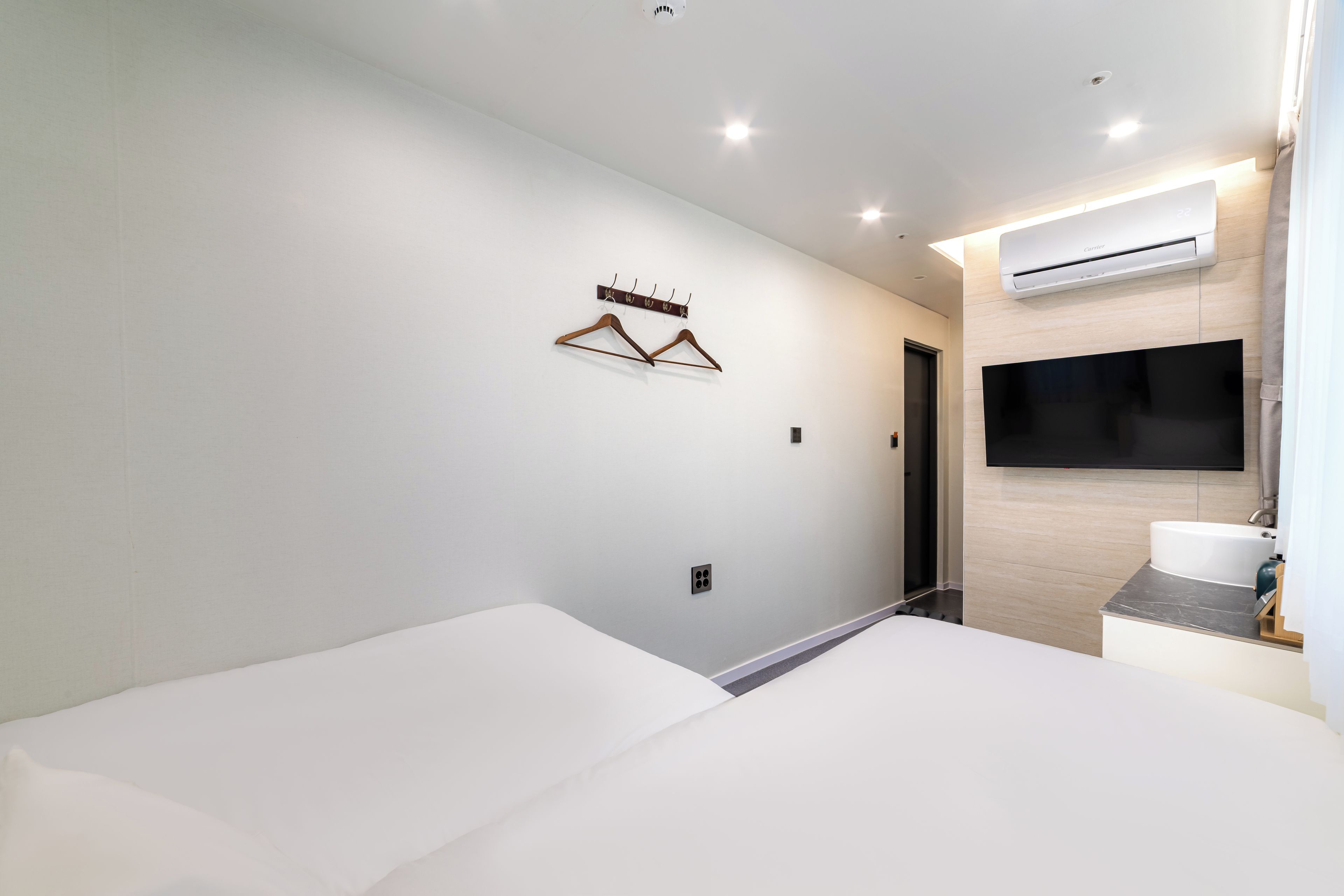 A hotel room with a bed, a TV mounted on the wall, and a coat rack with hangers.