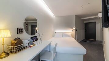A hotel room with a bed, a desk with a lamp, a mirror, and a door.