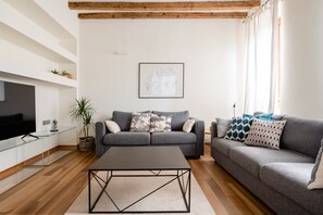 Ett modernt vardagsrum med en grå soffa, ett soffbord, en platt-TV och ett inramat konstverk på väggen.