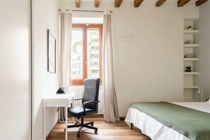 A bedroom with a bed, a desk with a chair, a window with curtains, and a shelf with plants. - 2 bedroom, 2 bathroom Apt + AC + FREE Garage (Milano)