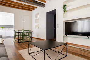 A modern living room with a flat-screen TV, a dining area with chairs and a table, and a kitchen in the background. - 2 bedroom, 2 bathroom Apt + AC + FREE Garage (Milano)