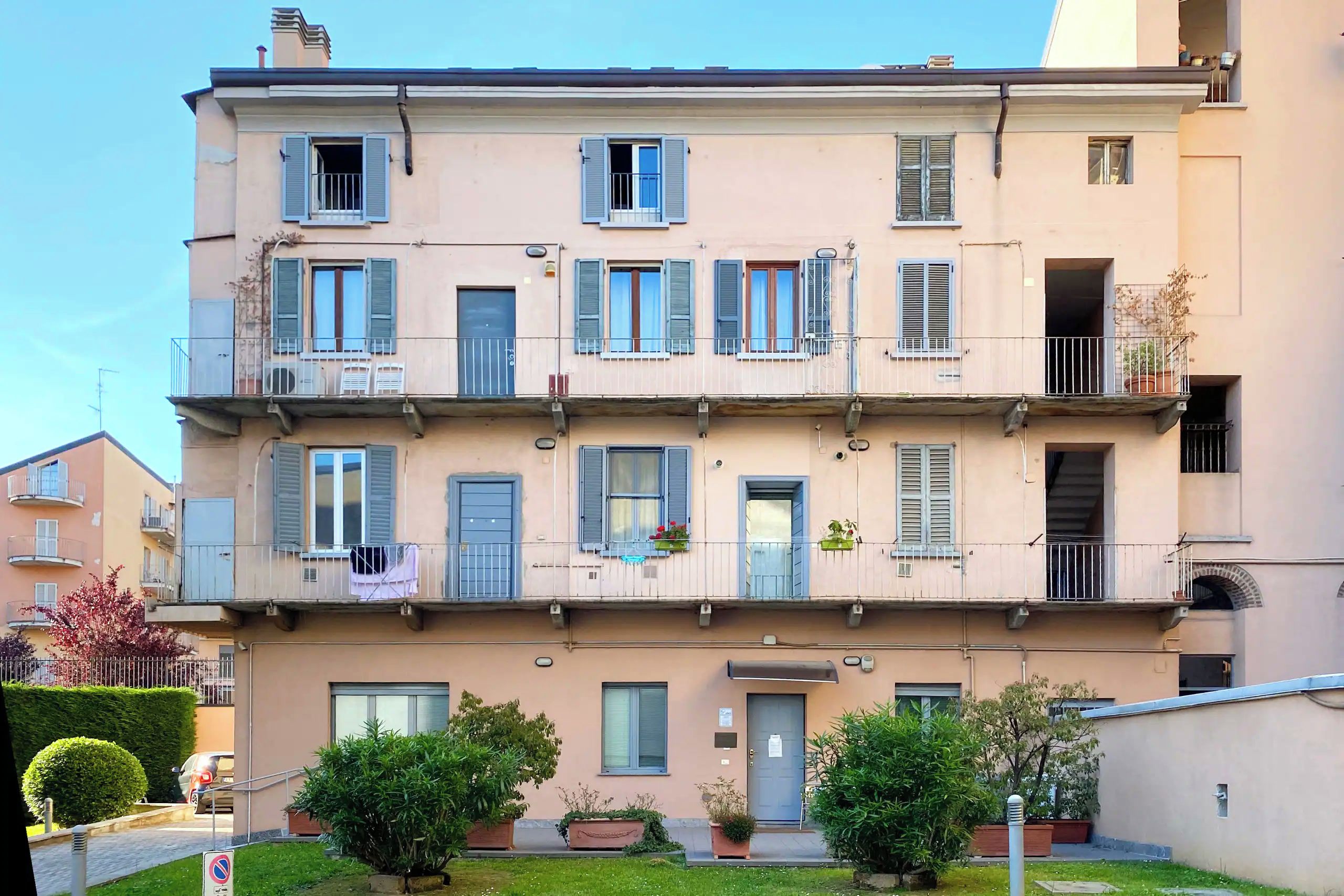 A multi-story residential building with balconies, a door, and potted plants.