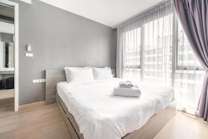 A modern hotel room with a large bed, a bedside table, a mirror, and a window with curtains. - Dazzle Residence Sukhumvit Bangkok (Krung Thep Maha Nakhon)