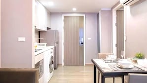 Une cuisine compacte équipée d’un lave-linge, un coin repas avec une table dressée pour deux personnes, et une porte fermée à l’arrière-plan.