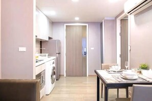 A compact kitchen with a washing machine, a dining area with a table set for two, and a closed door in the background. - Dazzle Residence Sukhumvit Bangkok (Krung Thep Maha Nakhon)