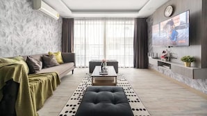 Un salon moderne comprenant un canapé, une table basse, un pouf et un téléviseur à écran plat fixé au mur.