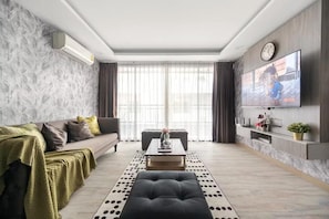 A modern living room with a sofa, coffee table, ottoman, and a flat-screen TV mounted on the wall. - Dazzle Residence Sukhumvit Bangkok (Krung Thep Maha Nakhon)