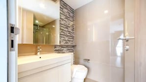 Une salle de bain moderne avec des toilettes blanches, un lavabo avec un miroir et un espace douche.