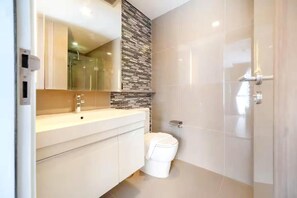 A modern bathroom with a white toilet, a sink with a mirror, and a shower area. - Dazzle Residence Sukhumvit Bangkok (Krung Thep Maha Nakhon)