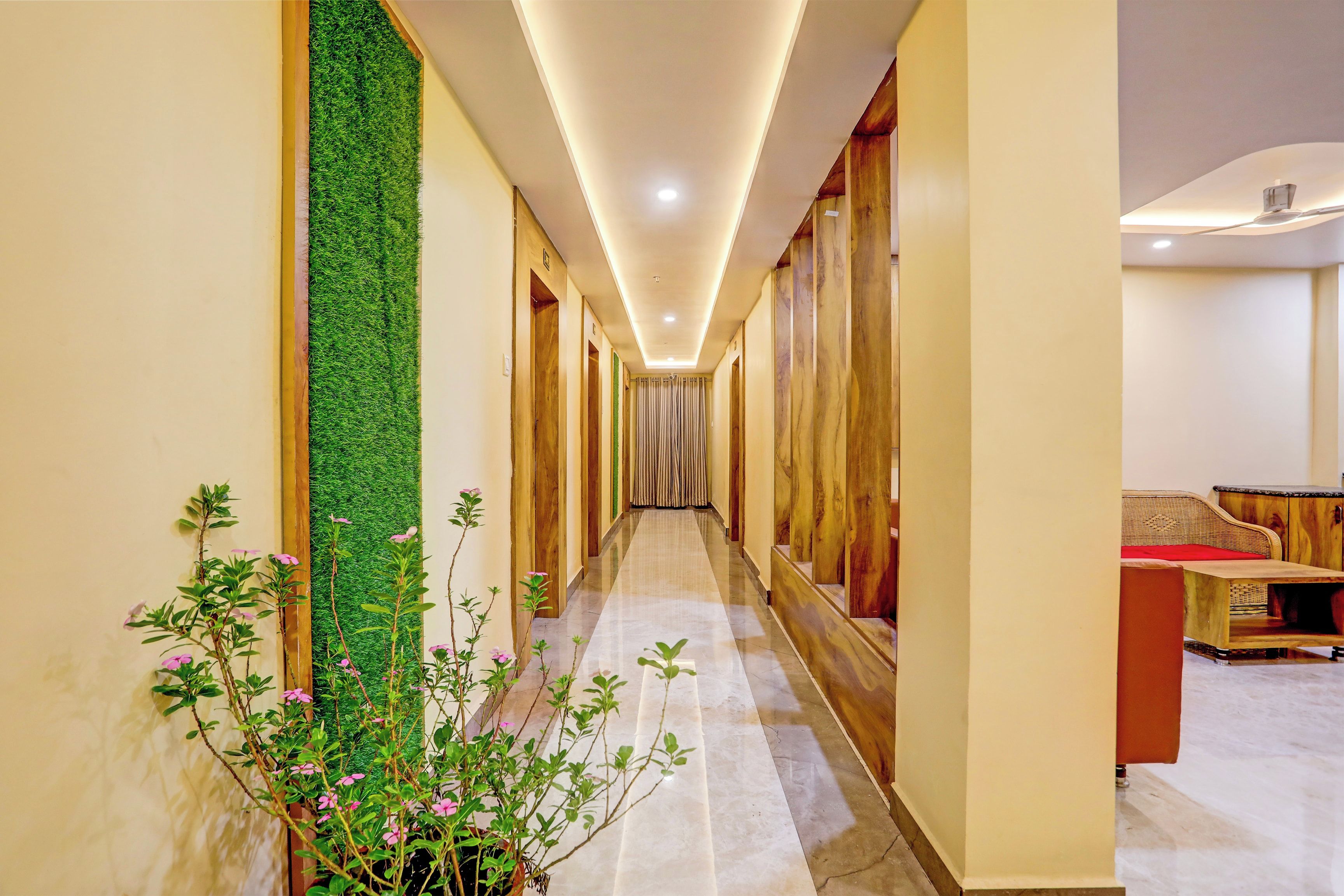 Un pasillo de hotel con un jardín vertical verde, puertas de madera y una zona de estar con un cojín rojo.