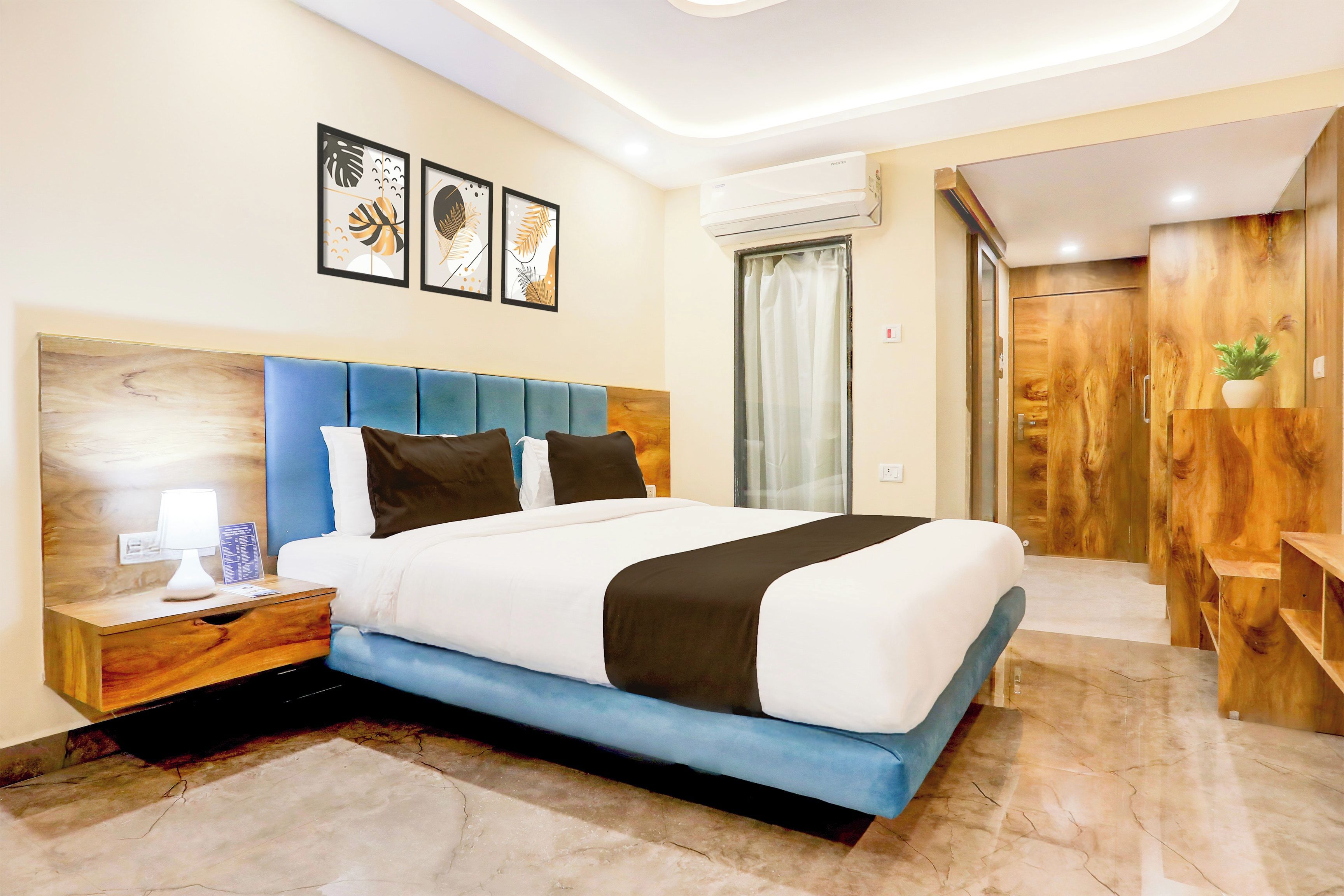 Une chambre d’hôtel comprenant un lit, une table de chevet, une lampe, un climatiseur fixé au mur et une armoire en bois.