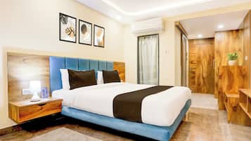 Une chambre d’hôtel comprenant un lit, une table de chevet, une lampe, un climatiseur fixé au mur et une armoire en bois.