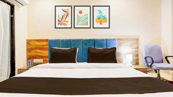 Quarto de hotel com uma cama, mesa de cabeceira, uma cadeira e três quadros na parede.