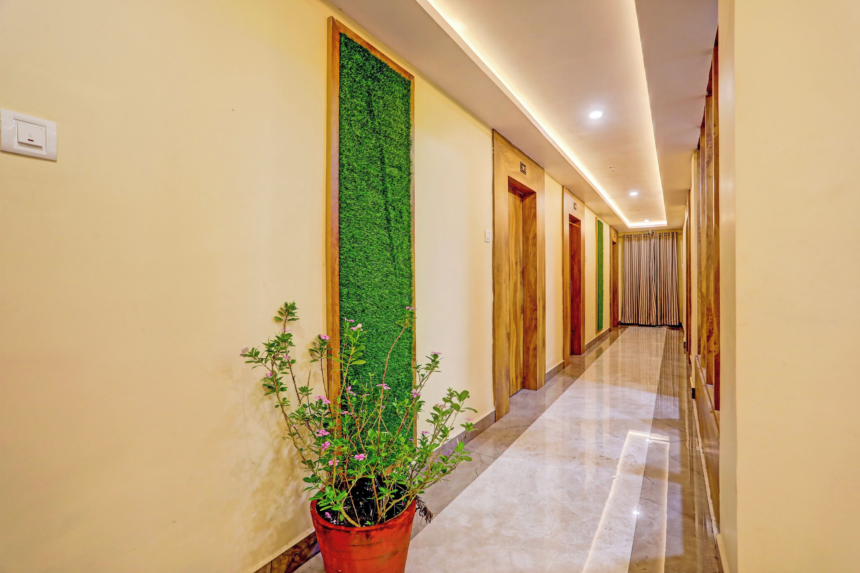 A hotel hallway with a green vertical garden, wooden doors, and a marble floor.