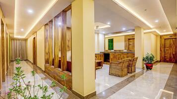 A hotel lobby with a marble floor, wooden paneling, a reception desk, and wicker furniture.