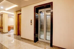A hallway with a marble floor, a wooden door with a number sign, and an elevator with a glass door.