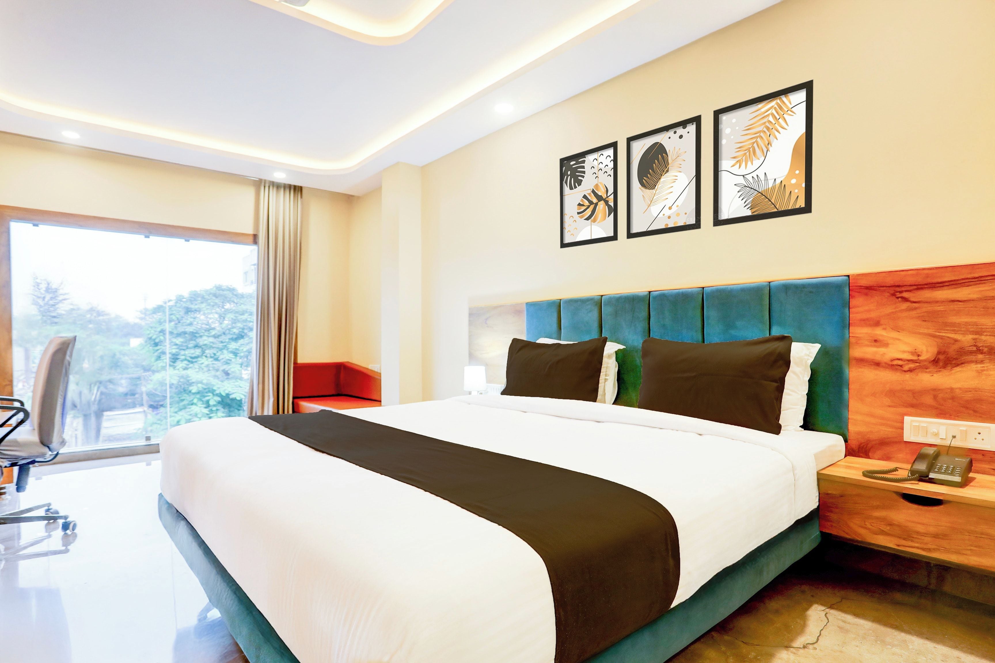 A hotel room with a large bed, a nightstand with a phone, and a window with a view of trees.