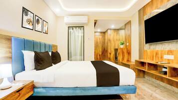 A modern hotel room with a large bed, a flat-screen TV, a desk with a lamp, and a wooden wardrobe.