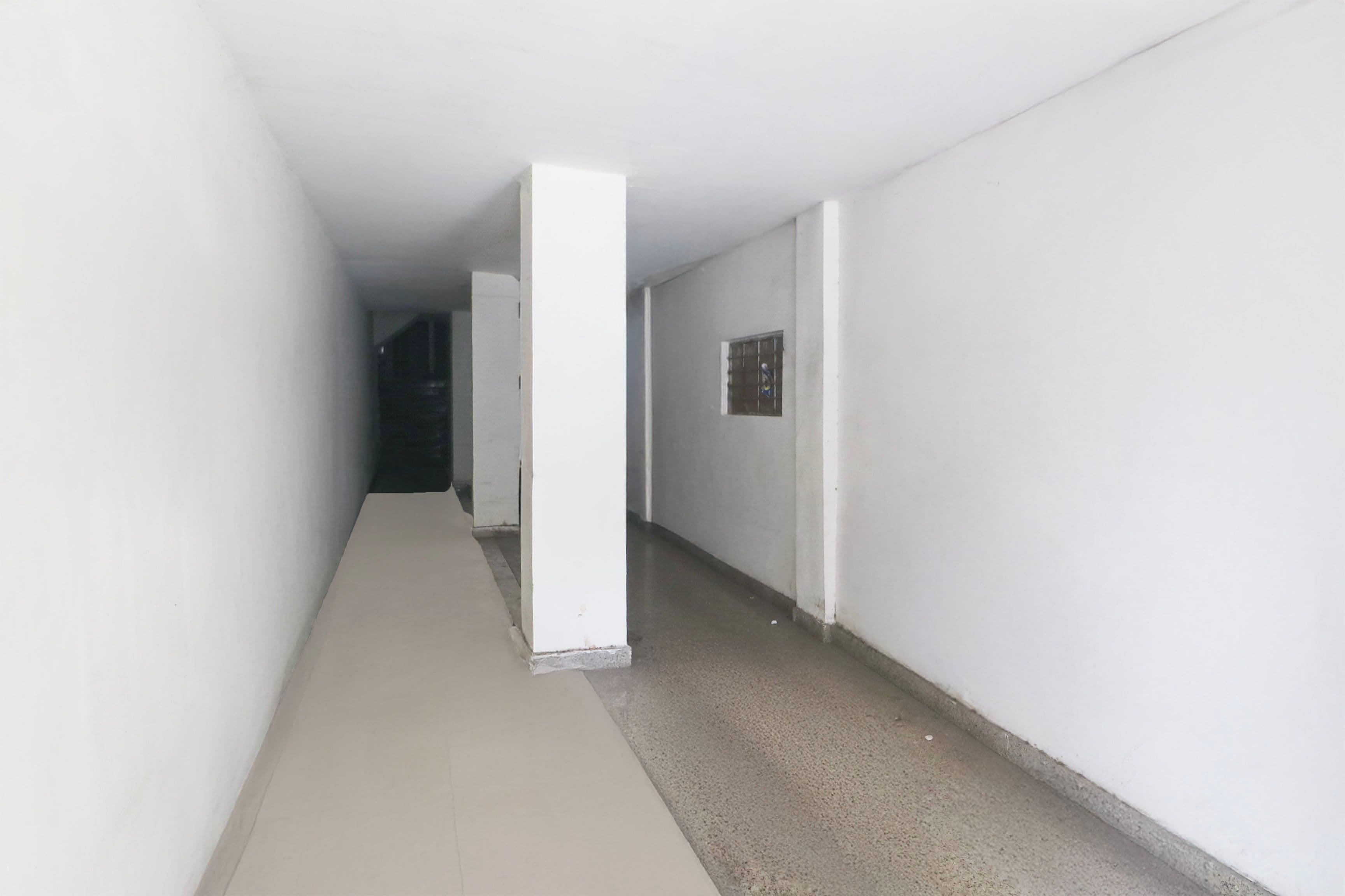 A corridor with white walls and a concrete floor, leading to a door at the end.