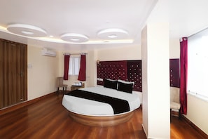 A hotel room with a bed, a wooden floor, a wardrobe, an air conditioning unit, and a window with curtains. - Super Townhouse Bank More Dhanbad (Dhanbad)