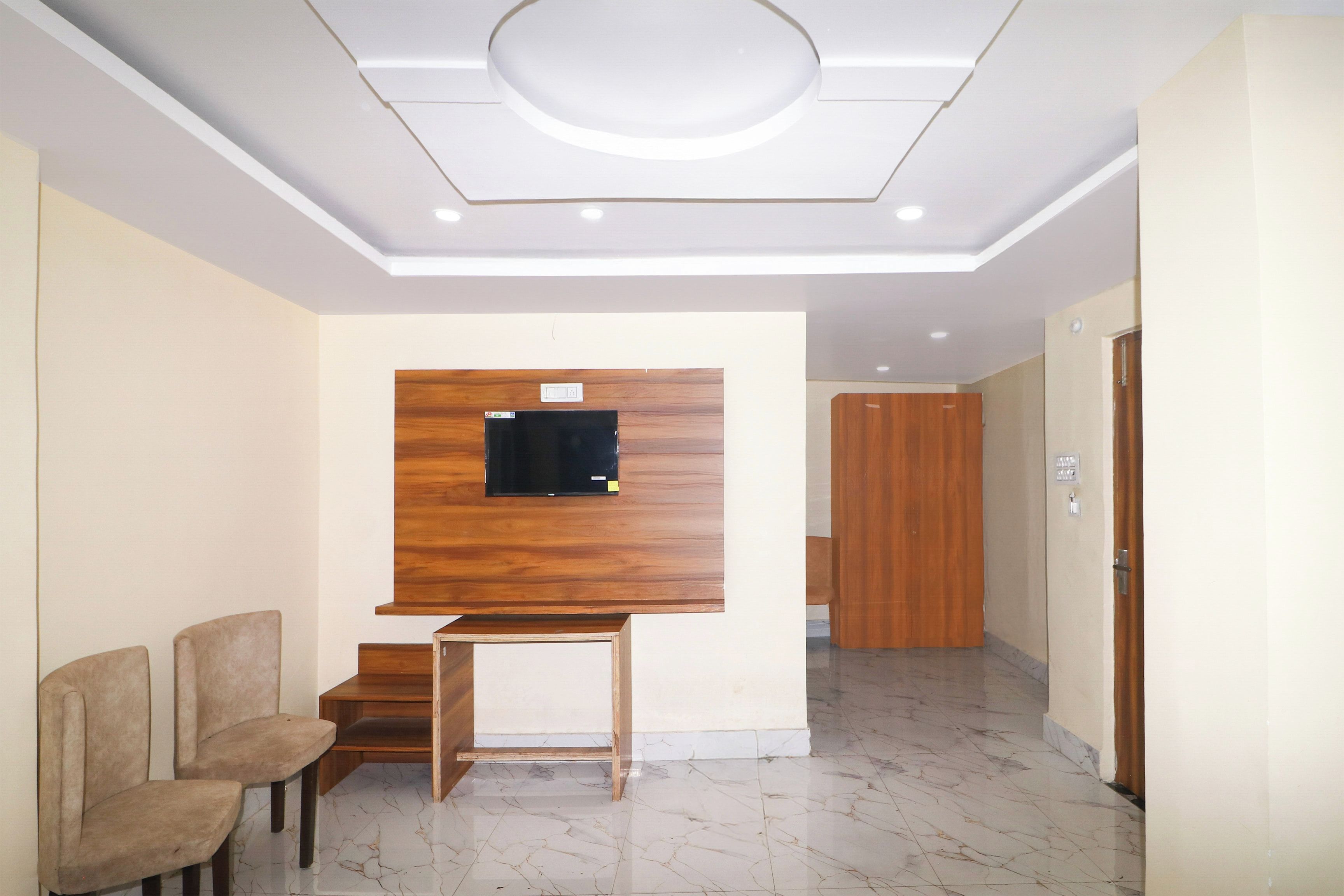 Eine Hotelhalle mit einer an der Wand befestigten Holz-TV, einer Sitzecke mit zwei Stühlen, einem Marmorboden und einer Holztür.