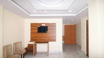 Un hall de hotel con una televisión de madera montada en la pared, una zona de estar con dos sillones, un suelo de mármol y una puerta de madera.