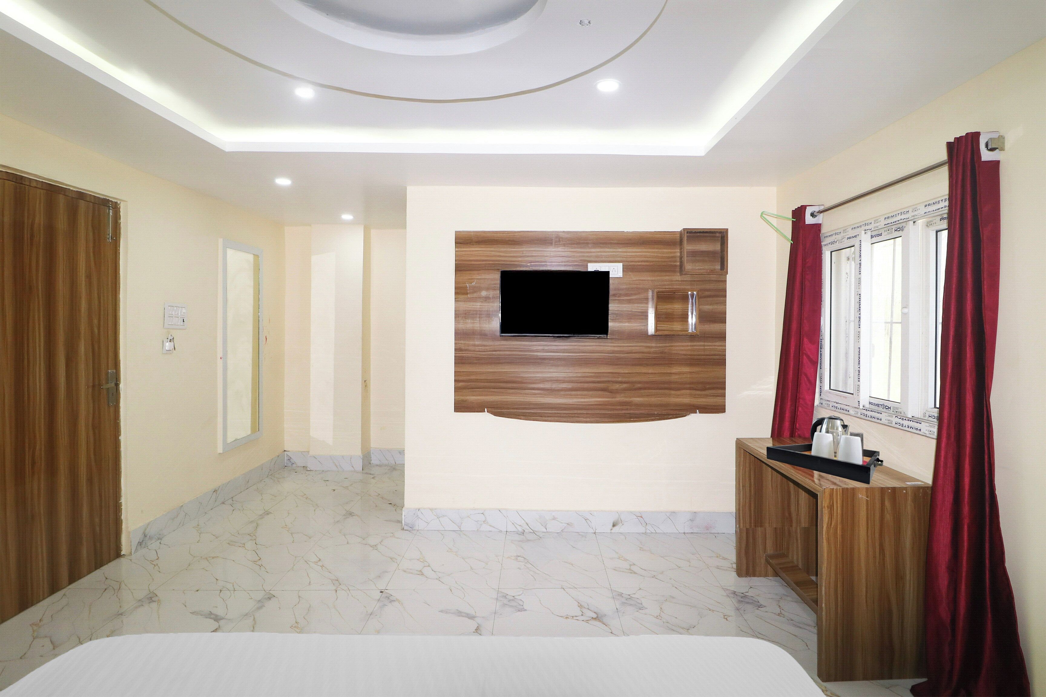 A hotel room with a wooden TV stand, a bed, a bathroom with a mirror, and a red curtain.