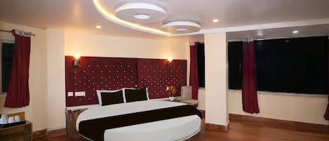 A modern bedroom with a circular bed, recessed ceiling lights, and a large window with curtains.