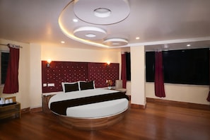 A modern bedroom with a circular bed, recessed ceiling lights, and a large window with curtains. - Super Townhouse Bank More Dhanbad (Dhanbad)