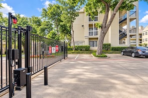 A gated parking area with a stop sign, a security gate, and a multi-story building in the background. - 1BR Condo Near Love Field and Medical District - Pool and Gated Parking (Dallas)