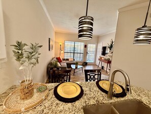 A modern kitchen with granite countertops, a sink, and a dining area with a table and chairs. - 1BR Condo Near Love Field and Medical District - Pool and Gated Parking (Dallas)