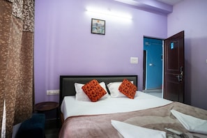 Camera d'albergo con un letto, un comodino, un tavolino e un quadro appeso al muro, oltre a una porta.