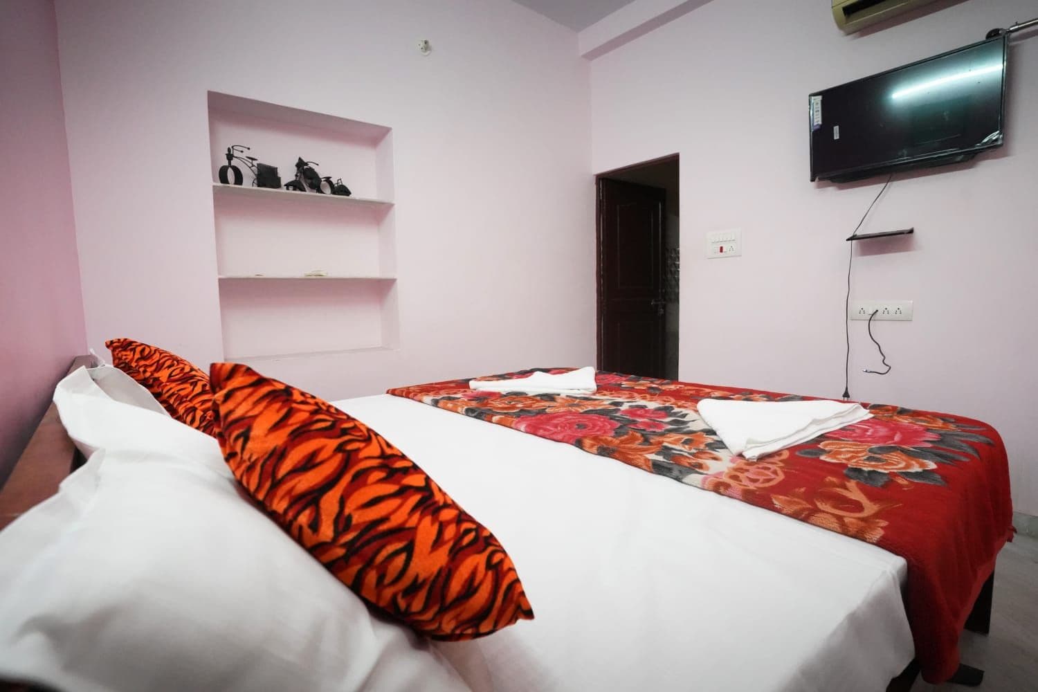 A hotel room with a bed, a television mounted on the wall, and a shelf with decorative items.