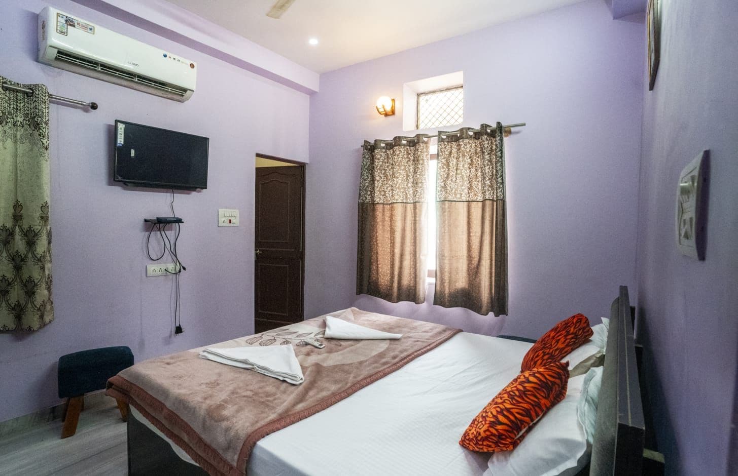 Un dormitorio con cama, televisor, aire acondicionado y ventana con cortinas.