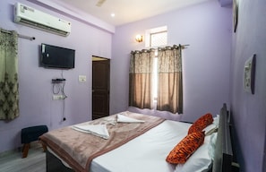 Una camera da letto con un letto, una televisione, un condizionatore d'aria e una finestra con tende.