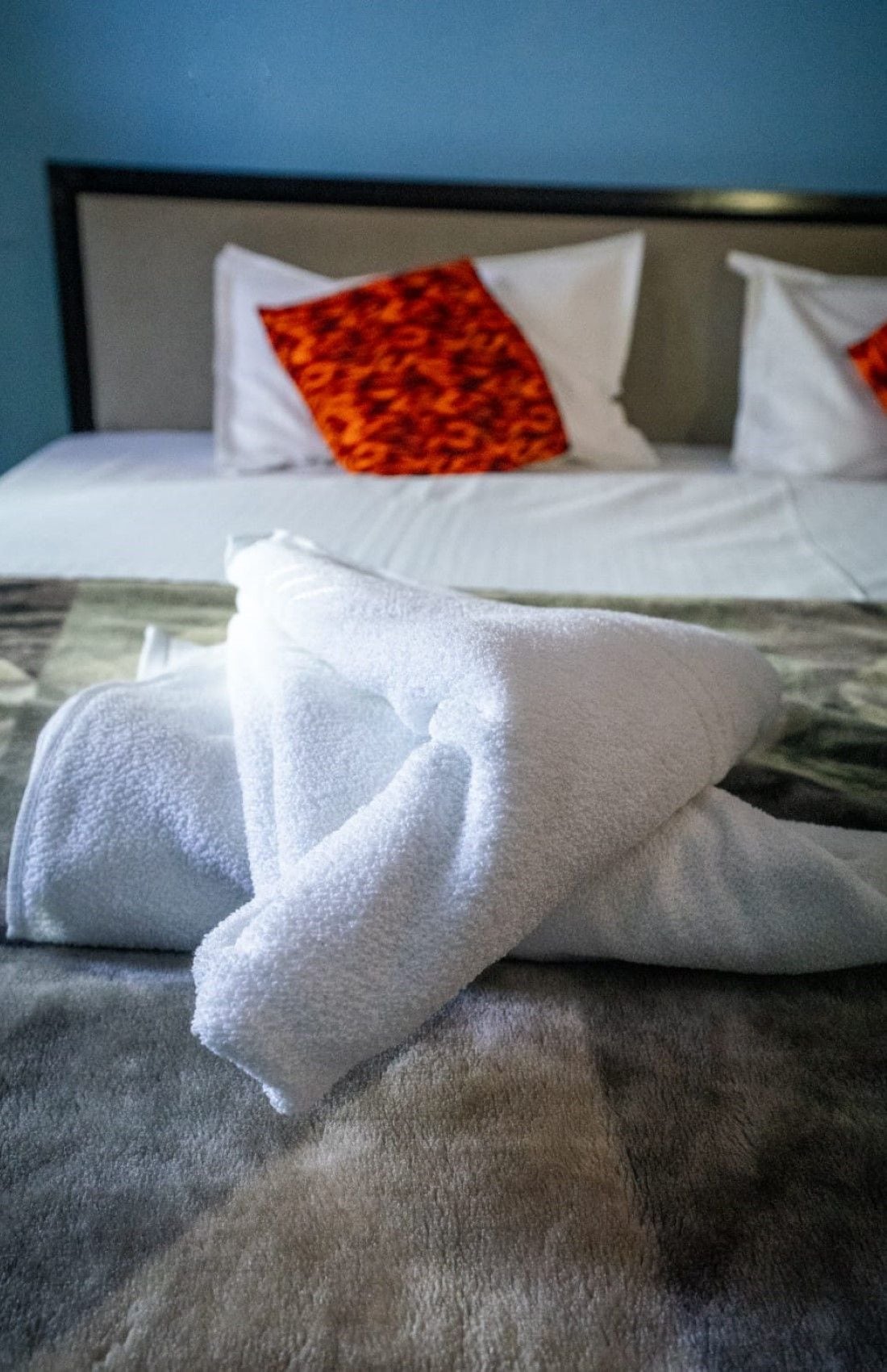 A neatly made bed with white linens and a folded towel on top.