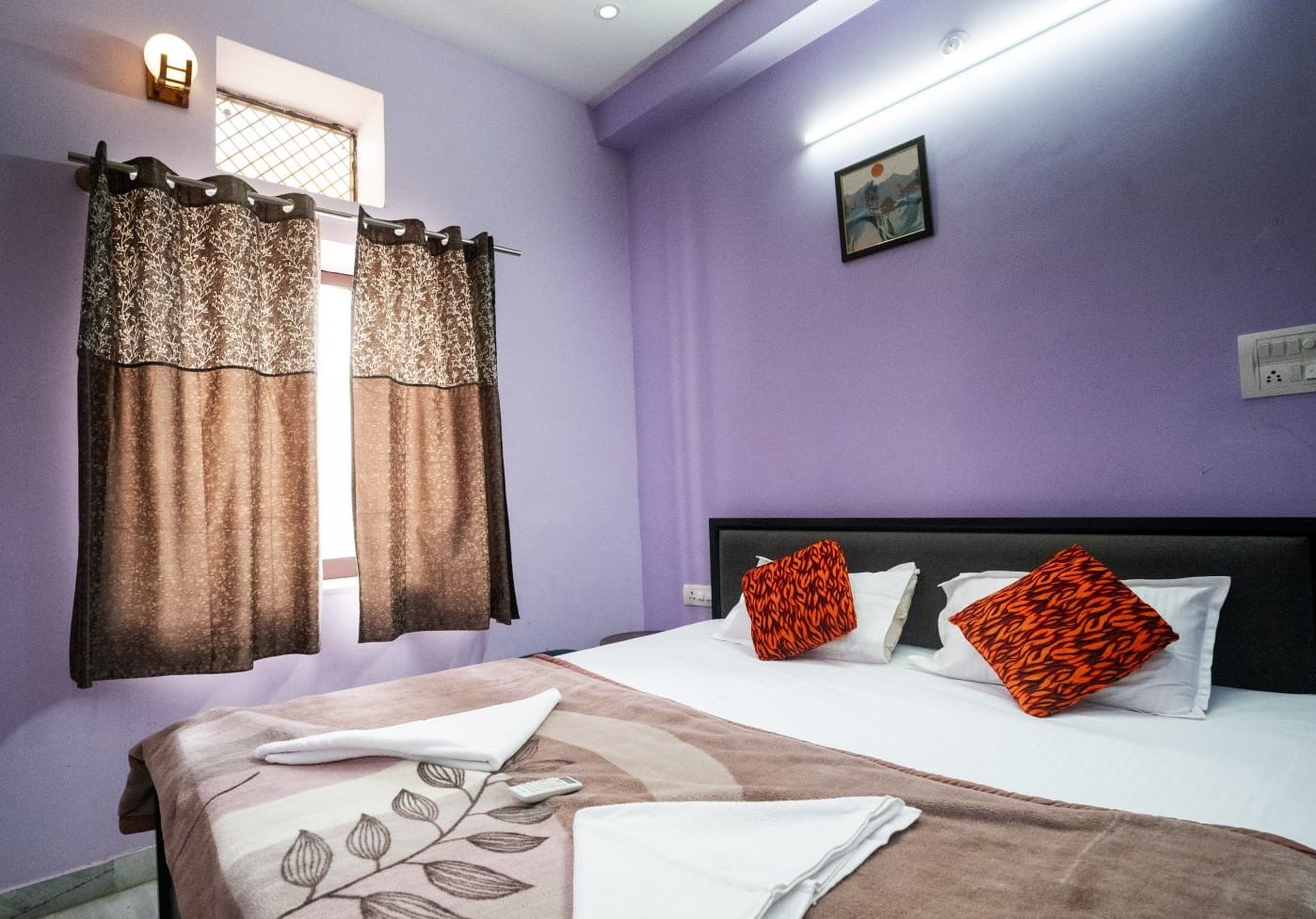 Un dormitorio con cama, cortinas, cabecero y una lámpara fijada a la pared.