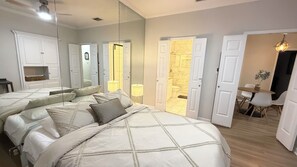 Un dormitorio con una cama grande, un espejo y un baño visible a través de una puerta abierta.