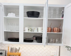 Ein Küchenschrank mit verschiedenen Gegenständen, darunter eine schwarze Schüssel, klare Gläser und Kupferkessel.