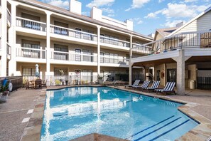 Un hotel de varios pisos con piscina, mobiliario exterior y balcones.
