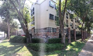 Un edificio residencial de varios pisos con fachada de ladrillo, ventanas grandes y entrada protegida por una reja.