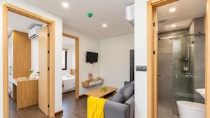 Una habitación de hotel moderna con sofá, una mesita, televisión, baño con ducha y retrete.