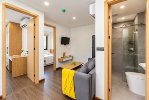 Una habitación de hotel moderna con sofá, una mesita, televisión, baño con ducha y retrete.