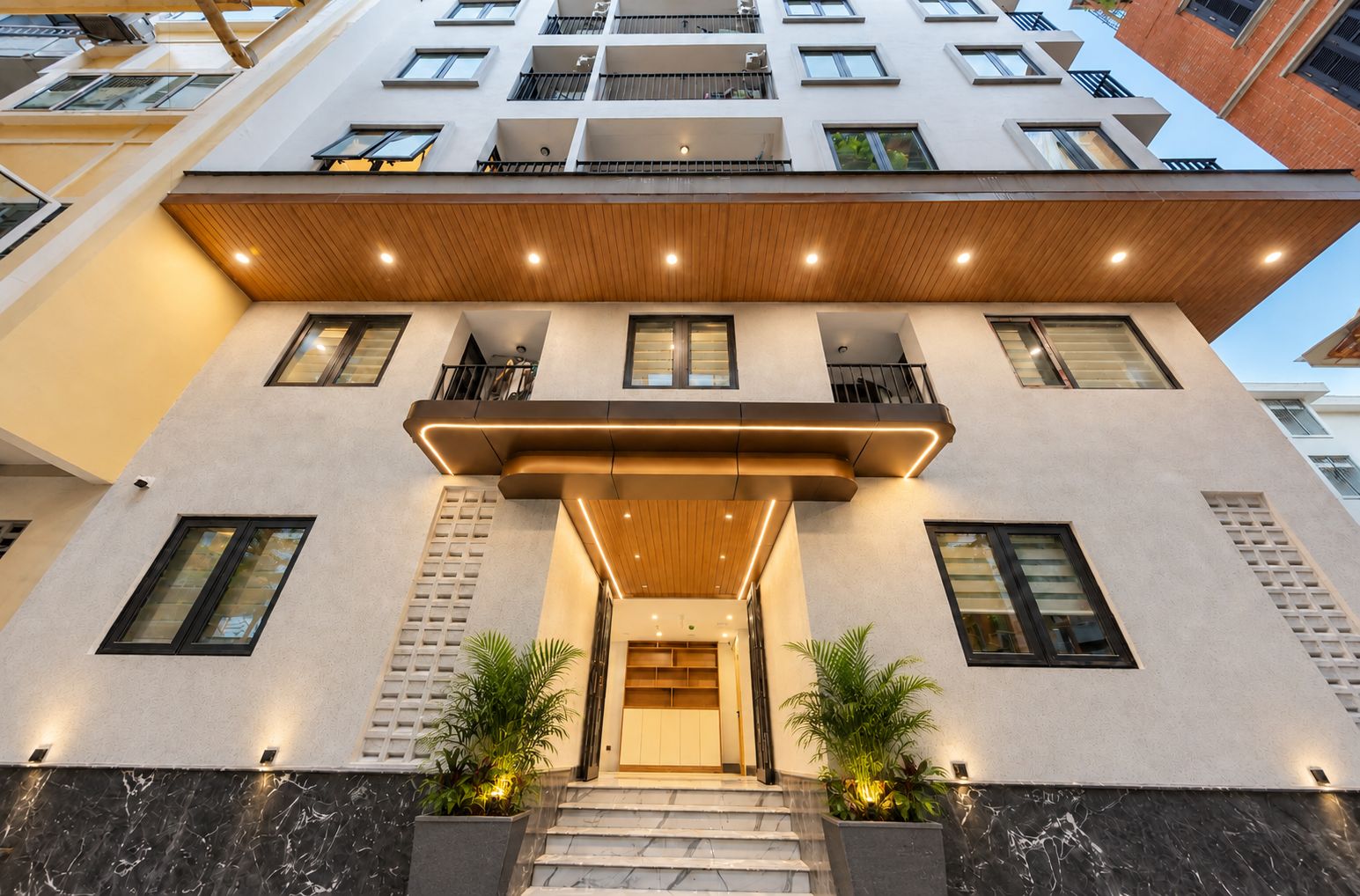 A modern building with a flat facade, multiple balconies, and a central entrance with steps.