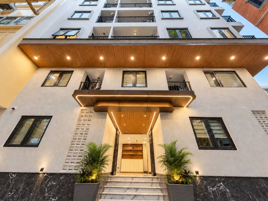 A modern building with a flat facade, multiple balconies, and a central entrance with steps.