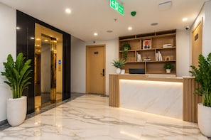 Zona de recepción de un hotel con suelo de mármol, mostrador de recepción, una planta y una estantería.