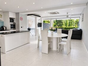 A modern kitchen with a dining area, white cabinetry, and a view of greenery outside. - 5 BDRM & BATHROOM Pool Villa. Golf Views, 7kms to Patong. Peaceful & private (Tambon Kathu)