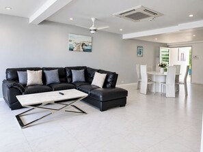A modern living room with a black leather sectional sofa, a wooden coffee table, and a dining area with white chairs. - 5 BDRM & BATHROOM Pool Villa. Golf Views, 7kms to Patong. Peaceful & private (Tambon Kathu)