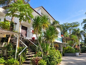 Un edificio de dos pisos con una escalera que conduce a un balcón, rodeado de exuberante vegetación tropical.